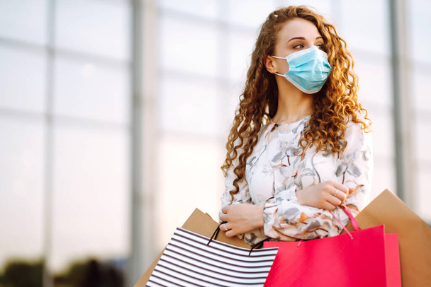 Woman in shopping. Young girl in protective sterile medical mask on her face with shopping bags enjoying in shopping. Concept of virus protection in the fashion, beauty and shopping industries. - Photo, image