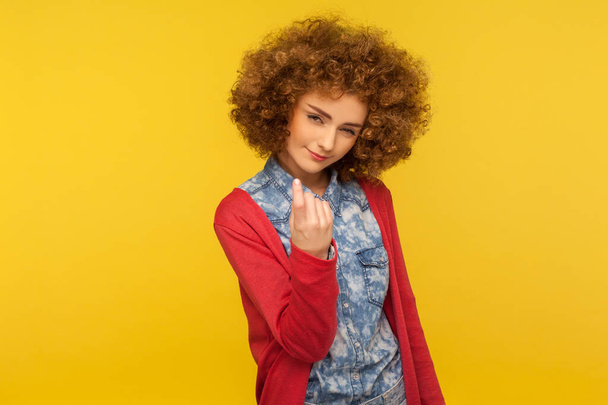 Come here, follow me! Portrait of pretty curly-haired woman looking playfully and calling with one finger, making beckoning gesture, inviting to come. indoor studio shot isolated on yellow background - Zdjęcie, obraz