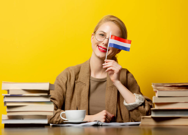 blonde vrouw met vlag van Nederland en boeken over gele achtergrond  - Foto, afbeelding