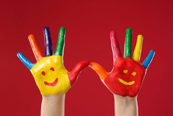 Kid with smiling faces drawn on palms against red background, closeup - Foto, Imagen