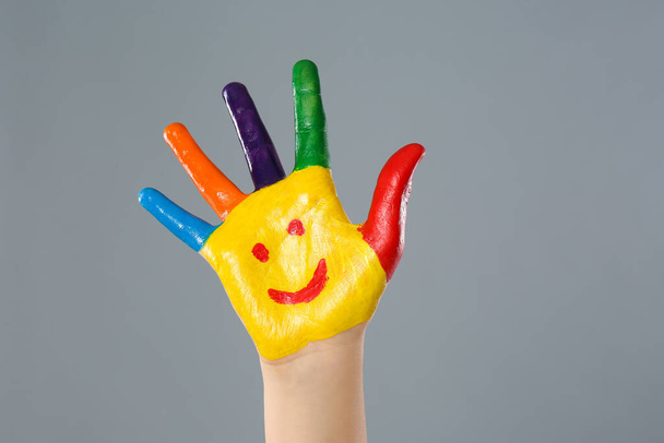 Kid with smiling face drawn on palm against grey background, closeup - Foto, immagini