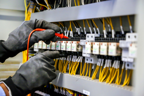 Digitális többméteres mérőberendezést alkalmazó villamosmérnök a fő áramelosztó tábla megszakítójánál lévő elektromos áram ellenőrzésére. - Fotó, kép