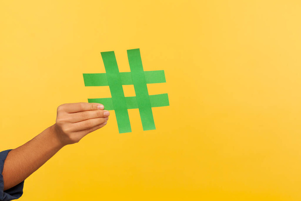 Blogging and social media trends. Closeup of hand holding hashtag sign, sharing tagged message, popular content, viral idea and comment on forum. indoor studio shot isolated on yellow background - Foto, imagen