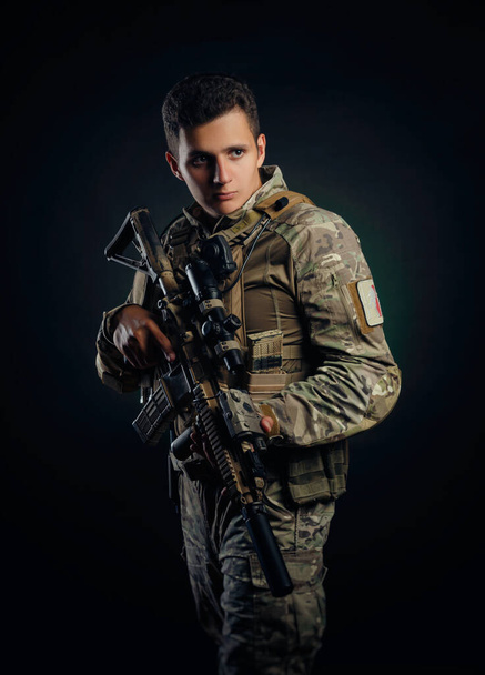 Julma mies armeijan ilmahaalareissa poseeraa ase kädessään tummalla pohjalla. - Valokuva, kuva