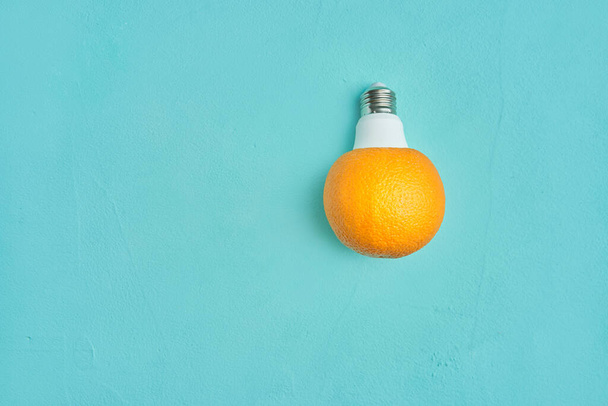 orange in a light bulb on a turquoise background. creative design concept - Zdjęcie, obraz