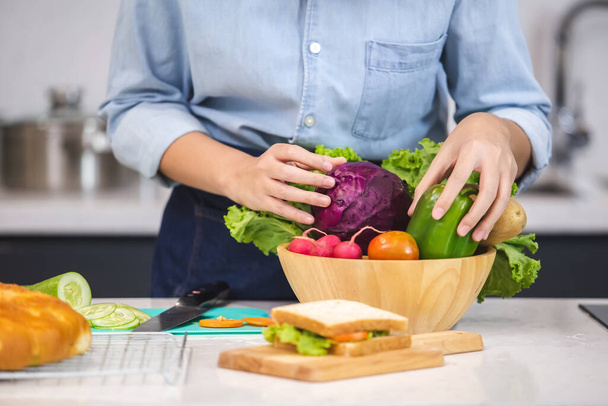 close-up hand van vrouw met groenten salade in houten kom op de kooktafel in de keuken. - Foto, afbeelding