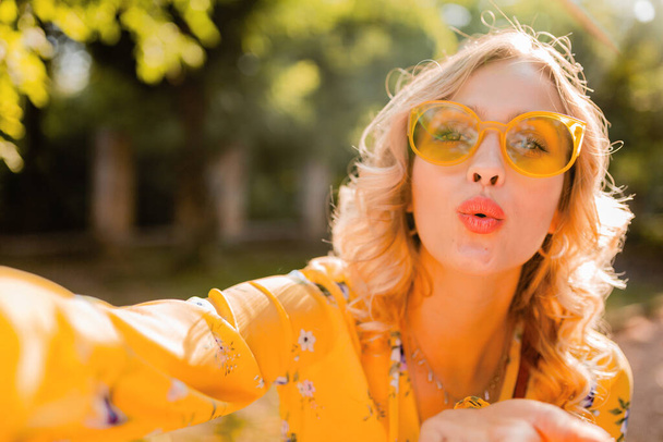 portrait of beautiful blond stylish woman in yellow blouse wearing sunglasses taking selfie photo, colorful summer fashion trend, bright sunny day, positive happy mood - Photo, Image