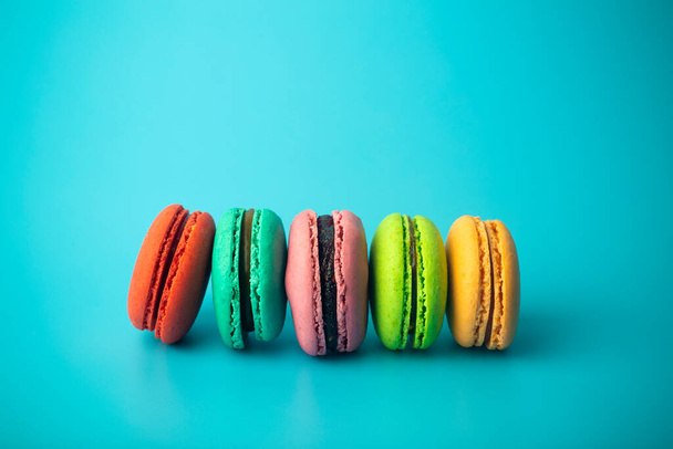 Цветной макарон (макароны) печенье на синем фоне. Яркая праздничная выпечка, десерты и сладости. Пекарный фон - Фото, изображение