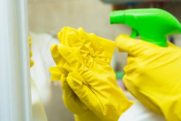 Девушка стирает зеркало в жёлтых перчатках. Девушка чистит зеркало моющими средствами
 - Фото, изображение