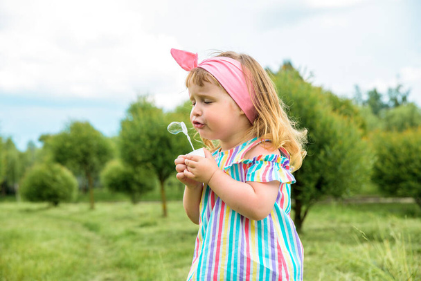 Cute little girl is blowing a soap bubbles.Fashionable baby girl in outdoors park, active games, runs. - Фото, изображение