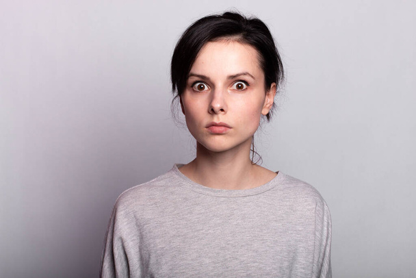 emotional  woman  in a gray t-shirt on a gray background - Photo, Image