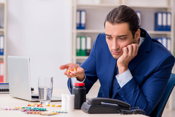 Junge männliche Angestellte und viele Pillen auf dem Schreibtisch - Foto, Bild