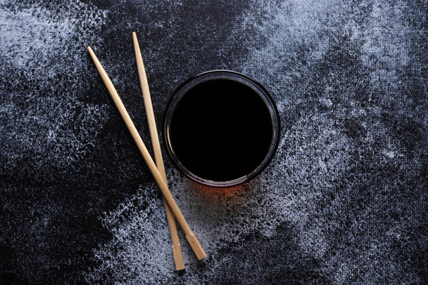 Sauce pour rouleaux de sushi et bâtonnets de bois sur un fond sombre, vue sur le dessus. Nourriture japonaise. - Photo, image