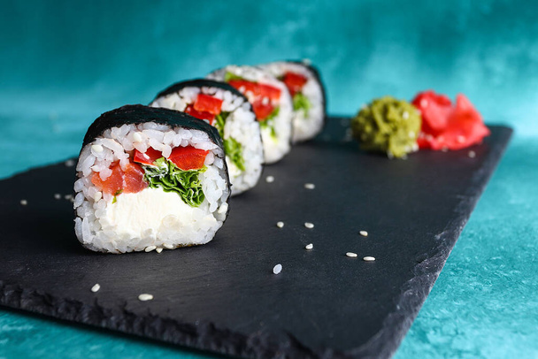 Sushi toczy się na tablicy obok imbiru i wasabi. Jedzenie japońskie. - Zdjęcie, obraz