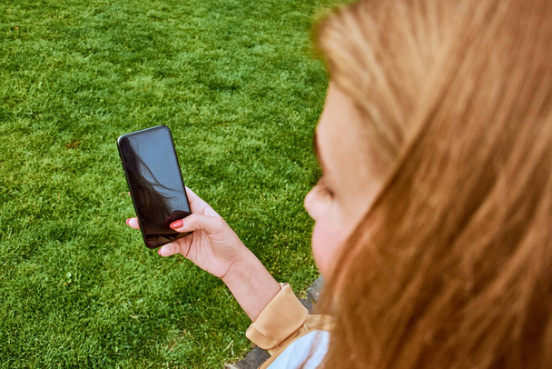 Close up of young woman using blank screen smartphone against grass background. - Zdjęcie, obraz