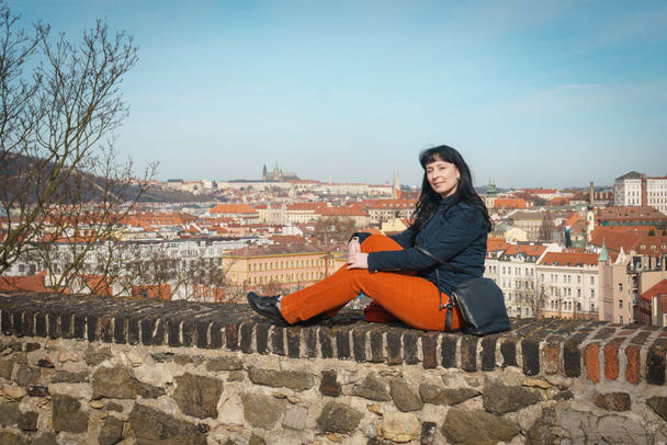 Девушка в ярких штанах сидит на стене Вышеградской смотровой площадки
. - Фото, изображение