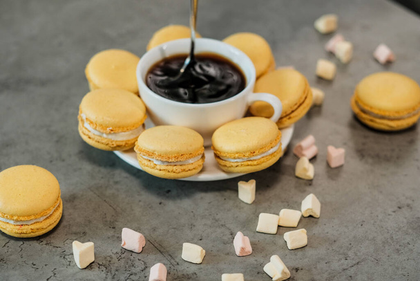 Hrst lahodné žluté francouzské Macarons na stole s šálkem kávy a marshmallow - Fotografie, Obrázek