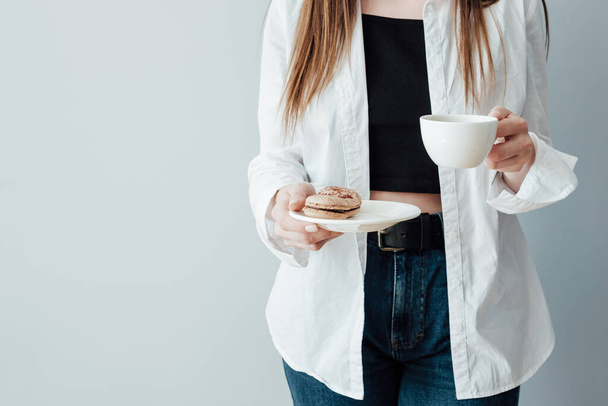 Camiseta chica de blanco y pantalones vaqueros sostiene taza de café y plato de macarrones franceses
 - Foto, imagen