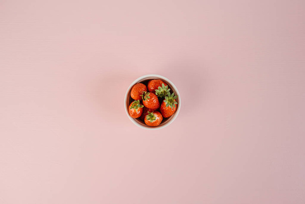 Flach auf einer Handvoll Erdbeeren, die auf dem rosafarbenen Hintergrundtisch liegen - Foto, Bild