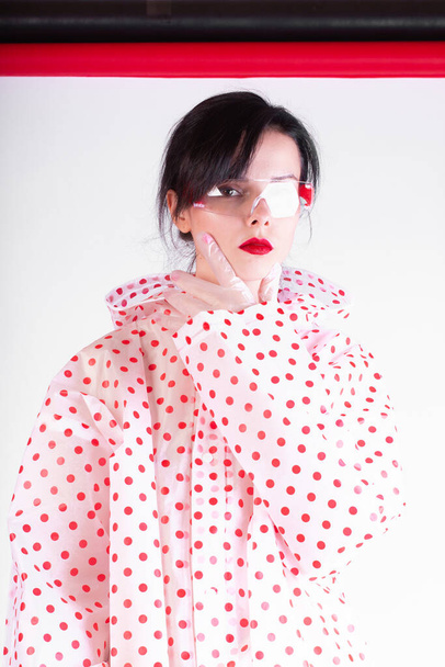beautiful woman with red lips in a raincoat and protective transparent glasses - 写真・画像