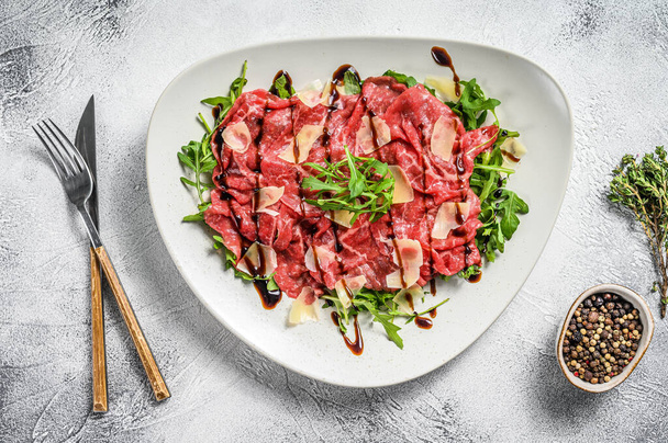 Beef carpaccio on white plate with parmesan cheese and arugula. Gray background. Top view - Photo, Image