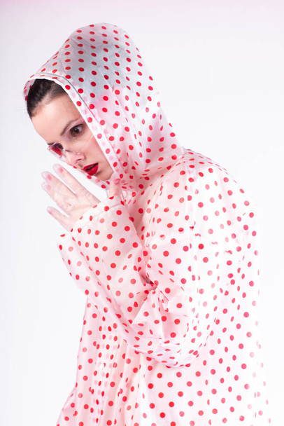 fashionable woman in a coat with red polka dots, transparent glasses, a light background - 写真・画像