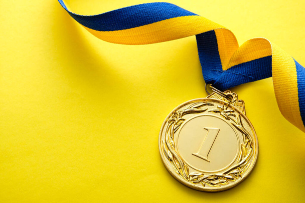 Kazanan ya da şampiyon için altın madalyon ya da mavi ve sarı kıvrımlı bir kurdele üzerinde koşan ve kopyalama alanı olan sarı bir arka plan. - Fotoğraf, Görsel