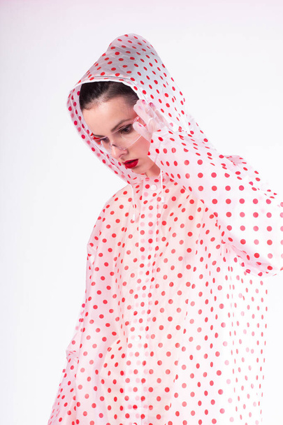 fashionable woman in a raincoat in red polka dots, transparent glasses and gloves, a light background - Foto, imagen