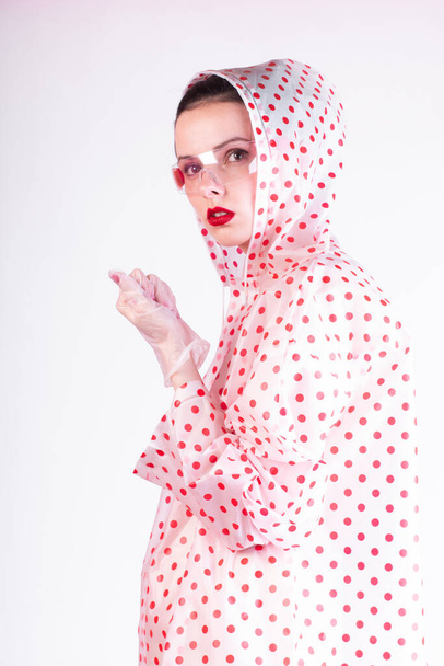 fashionable woman in a raincoat in red polka dots, transparent glasses and gloves, a light background - Photo, image