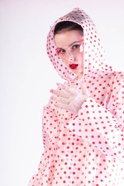strange fashionable woman in a coat with red polka dots, transparent glasses, a light background - Photo, Image