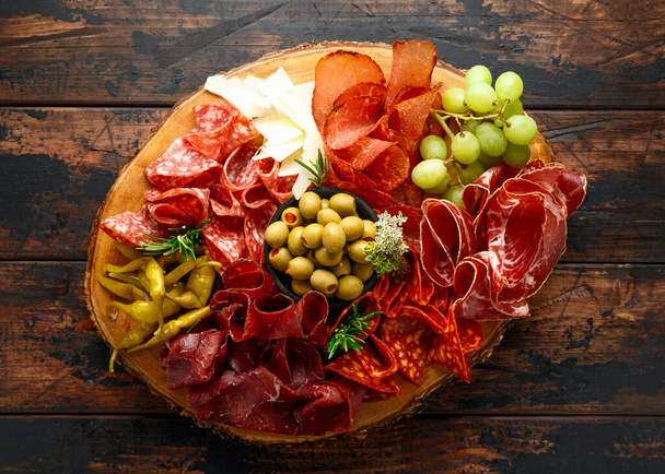 Droog gefermenteerd rundvlees en varkensvlees cocktailselectie met salami, chorizo, kaas, olijven en druiven geserveerd op houten plank. - Foto, afbeelding