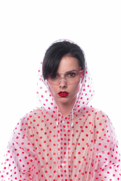 woman in a raincoat with red polka dots, transparent safety glasses, strange fashionable style - Zdjęcie, obraz