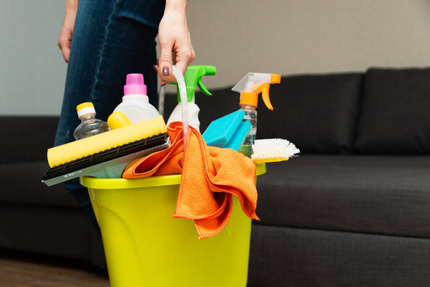 Dziewczyna trzyma detergenty w wiadrze na tle. Kobieta jest gotowa posprzątać dom. Sprzątanie w domu. Sprzątać i myć dom. Gospodyni domowa sprząta.. - Zdjęcie, obraz