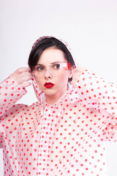 woman in a raincoat with red polka dots, transparent safety glasses, red lips - Photo, Image