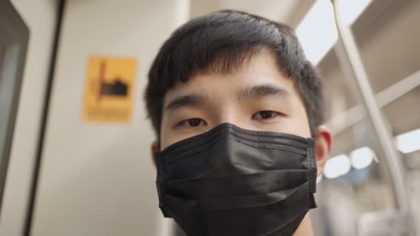 Asian male wearing black mask look at camera then look out the window, standing next to train door. covid-19 pandemic disease, public transport, after tiring day at work, new normal life rush hour - Footage, Video