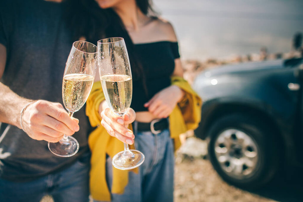 Travel, tourism - Man and woman drink champagne near the water at a folding portable table. Picnic near the water. Couple going on Adventure. Car travel concept. - Photo, image