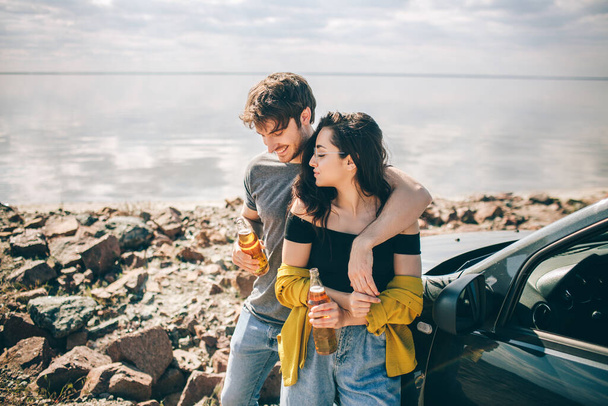 Travel, tourism - Man and woman drink champagne near the water at a folding portable table. Picnic near the water. Couple going on Adventure. Car travel concept. - Photo, Image