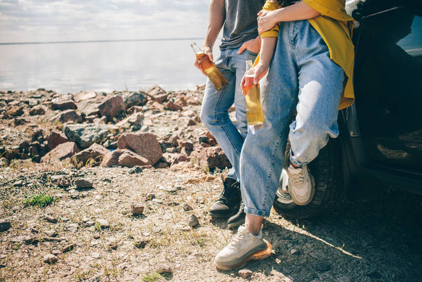 Travel, tourism - Picnic near the water. Couple going on Adventure. Car travel concept. Man and woman drink beer - 写真・画像