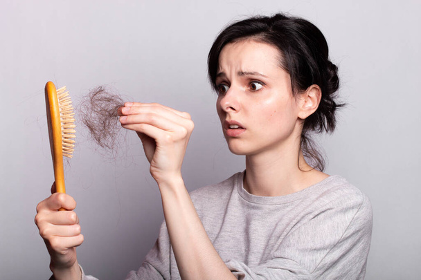 sad woman with a comb and a scrap of hair in her hands, the problem of hair loss - Foto, Bild