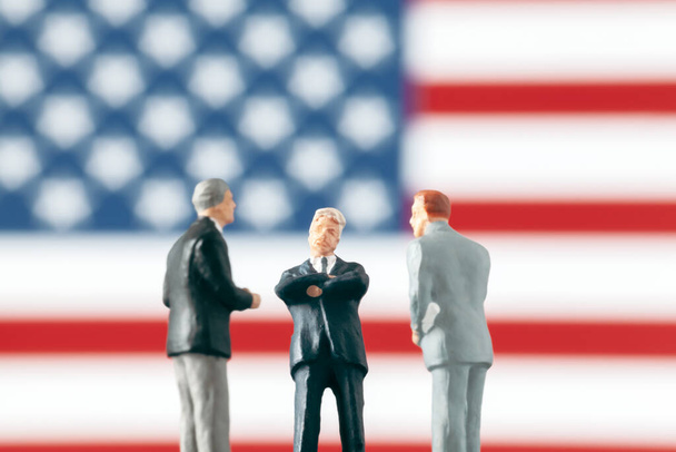 Acuerdo o negociación en política: Figuras en miniatura discutiendo sobre un tema frente a la bandera desenfocada de los Estados Unidos de América. Concepto de mundo de los negocios con hombres de negocios
. - Foto, Imagen