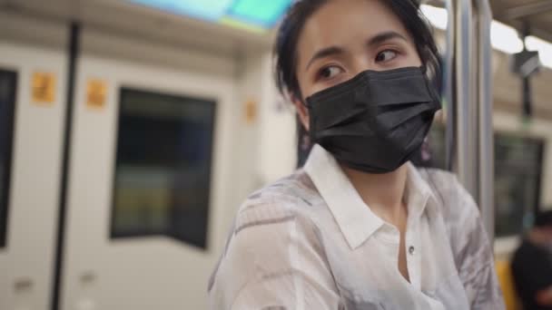 Aziatisch vrouw in zwart beschermend masker kijken naar camera, vasthouden aan de paal staan in het centrum van de trein auto, metro station, covid-19, sociale afstand concept, Nieuwe normale levensstijl, SLOW MOTION  - Video