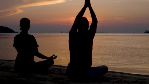 Het silhouet van de mens en de vrouw zit in lotuspositie, mediteert en doet yoga oefeningen bij zonsondergang - Video