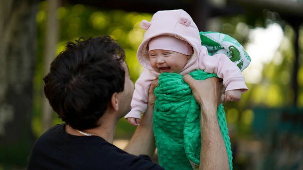 Tata trzyma w ramionach nowonarodzoną córkę. Dziecko w zielonym romper śmieje się radośnie - Zdjęcie, obraz