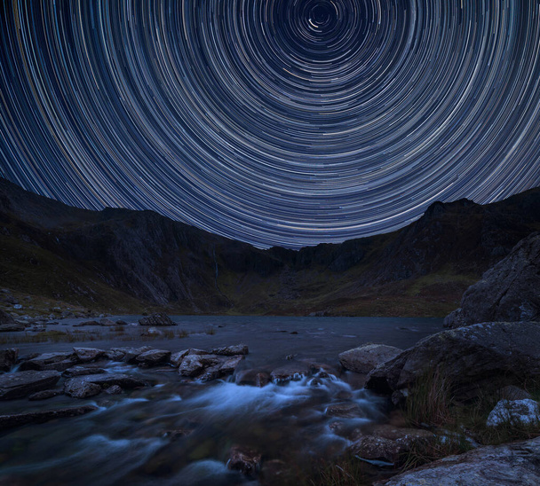 Digitaalinen komposiitti kuva tähti polkuja ympäri Polaris upea elinvoimainen maisema kuva joki virtaa alas vuorijono
  - Valokuva, kuva