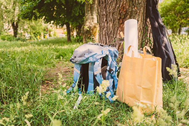 Рюкзак и спортивный инвентарь лежат на траве возле дерева. Перерыв на отдых во время пешеходной поездки
 - Фото, изображение