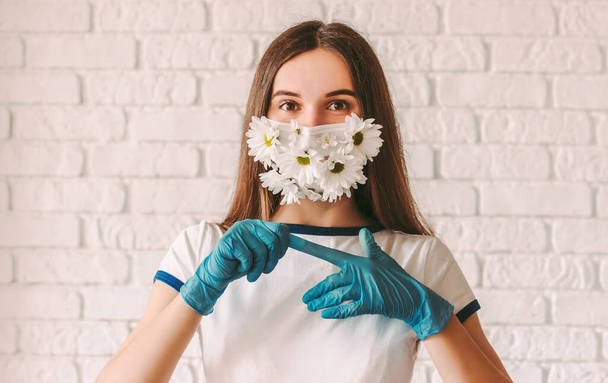 Portrait young girl doctor in medical face mask with flowers remove protective gloves from hands. Happy beautiful woman in protective mask celebrate end of coronavirus COVID-19 fight, take off gloves - Fotoğraf, Görsel