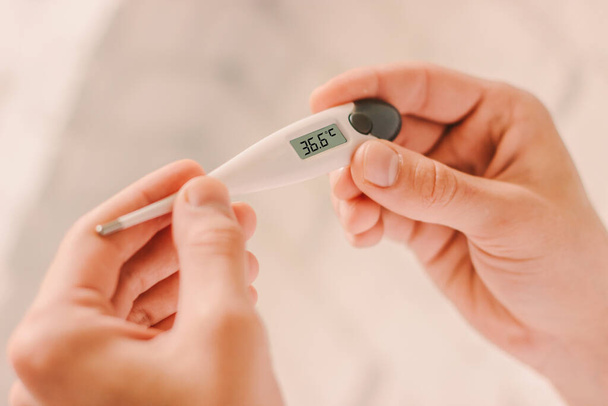 Closeup of doctor looking at electronic thermometer with healthy normal 36.6 temperature. Man patient holding digital thermometer in hands. Coronavirus COVID-19 diagnosis. Body temperature measurement - Φωτογραφία, εικόνα