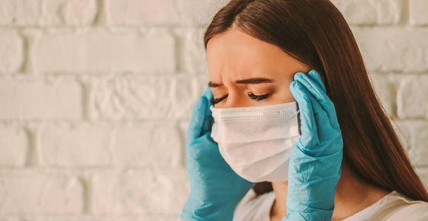 Exhausted stressed girl female doctor in protective mask on face and medical gloves suffering from headache. Tired sick woman in medical face mask and gloves. Coronavirus COVID-19 symptoms. High fever - Fotoğraf, Görsel