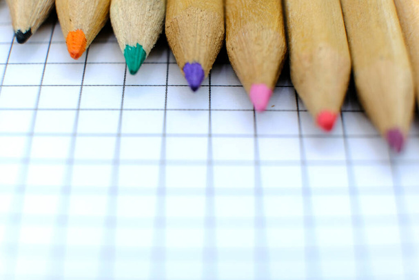 Крупним планом набір різнокольорових олівців на картатому паперовому аркуші ноутбука для малюнка. Повернутися до концепції школи. Копіювати простір, без людей. Невелика глибина різкості
 - Фото, зображення