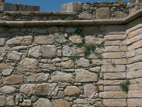 Old, rough, exterior stone wall of Portuguese castle with grass growing in cracks - Fotó, kép